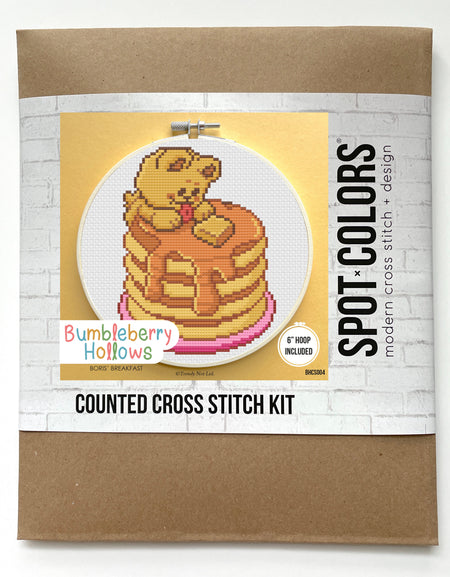 Cross stitch kit packaging with a bear on pancakes design on a white background