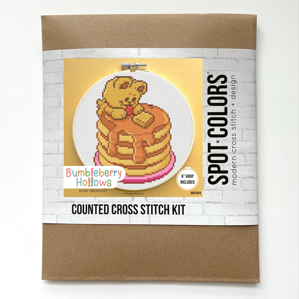 Cross stitch kit packaging with a bear on pancakes design on a white background