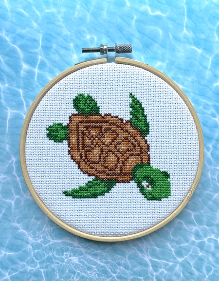 Cross-stitched turtle design in a hoop on a blue water-like background
