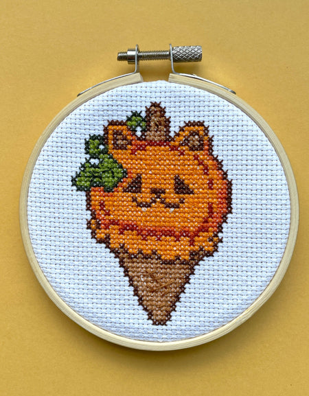 Cross-stitched design of a cat-shaped ice cream cone on a beige background