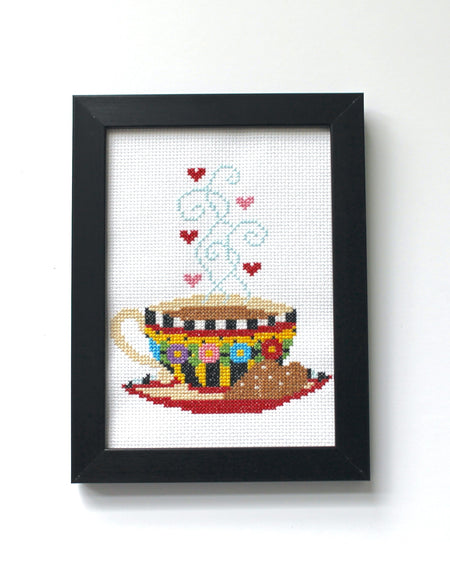 Framed cross-stitched artwork of a teacup with hearts on a white background